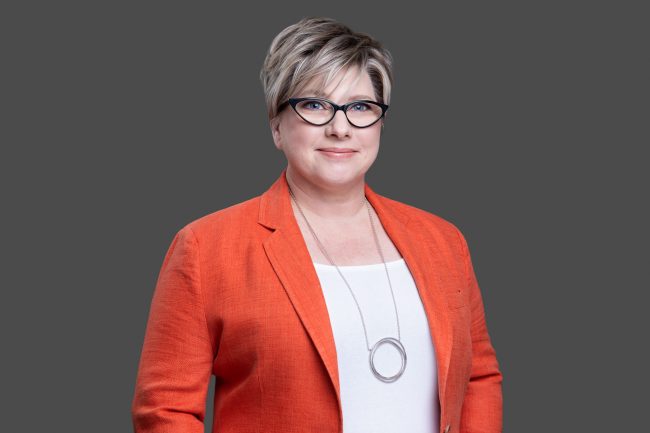 Dr Elena Rudnik from Resolve Mediation smiling in a professional portrait photo against a plain dark grey background.